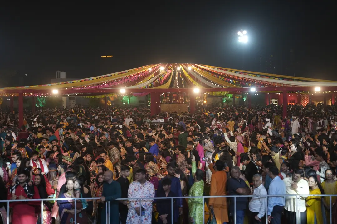 A packed garba floor under the canopy lights, seen from the back of the crowd