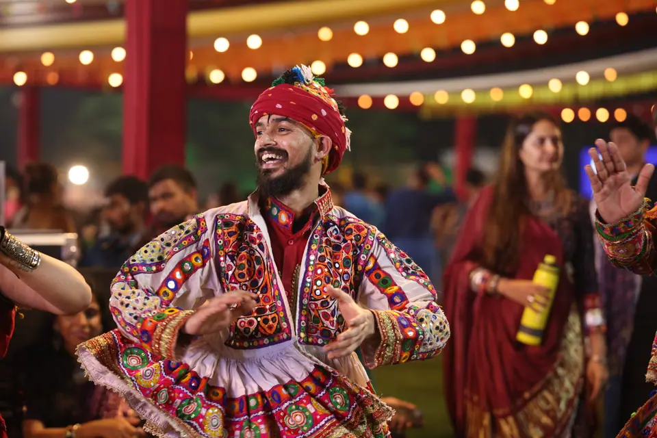 A man in a red turban and embroidered kediyu dancing and grinning