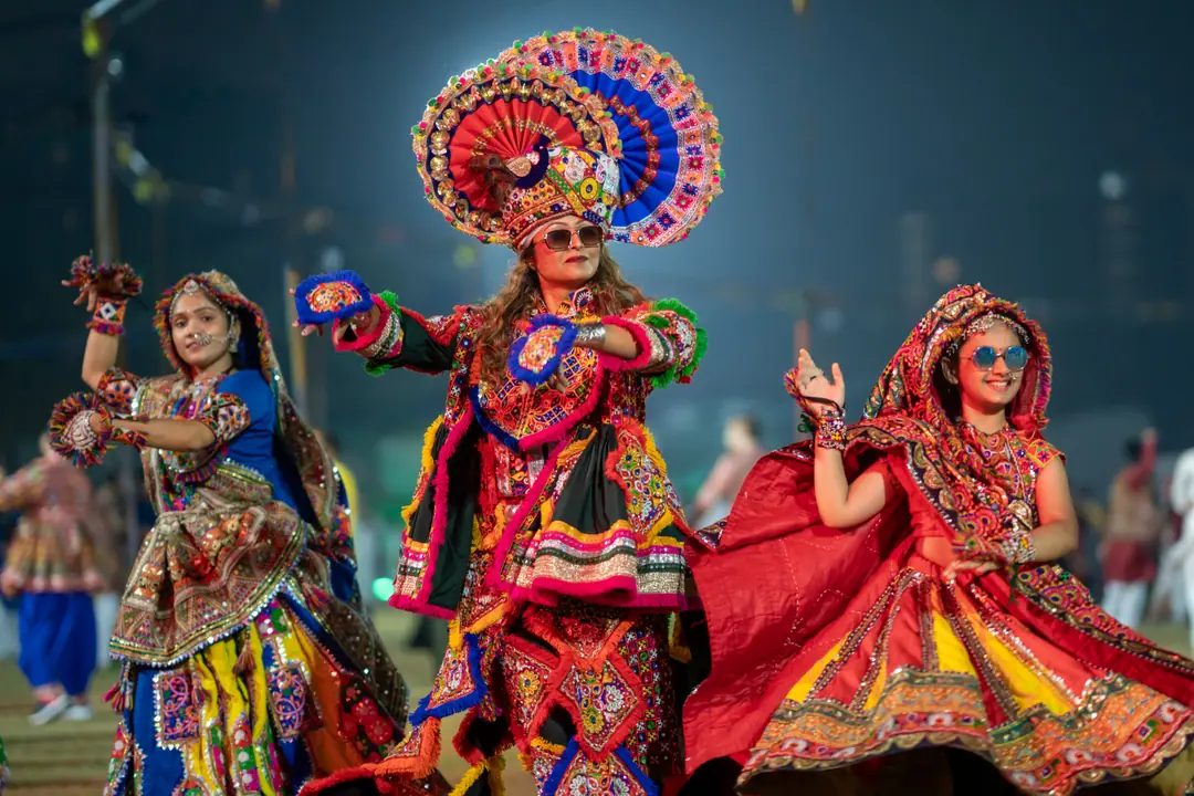 Three dancers in mirror-work chaniya cholis mid-garba, one in a tall peacock-fan headdress