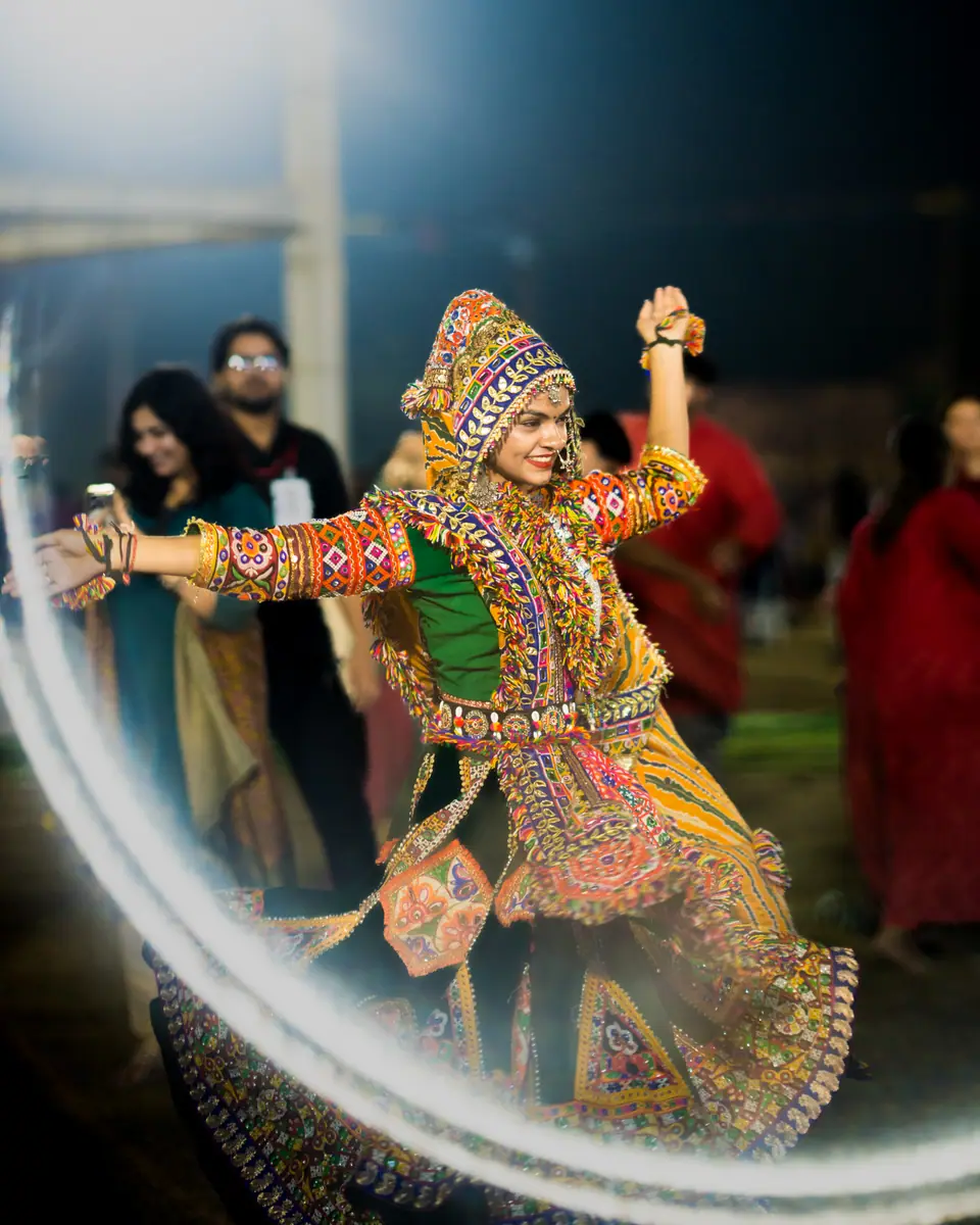 A dancer in a mirror-work hood and choli, arms wide mid-step
