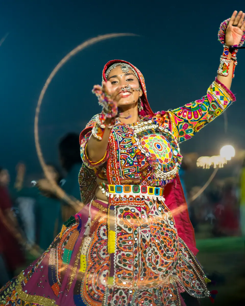 A smiling dancer in a mirror-work choli reaching toward the camera